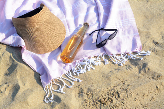 Pink Blanket With Stylish Visor Cap, Sunglasses And Bottle Of Beer On Sandy Beach, Above View