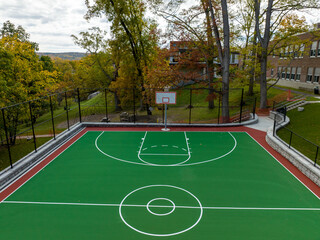Aerial photo of a green and red outdoor basketball court at school playground.  Court includes retaining walls and black vinyl coated chain link fence.	
