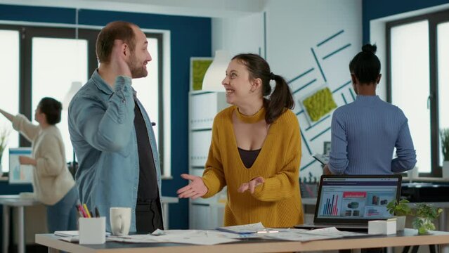 Smiling coworkers in startup office doing high five hand gesture celebrating good sales and high profit standing at desk. Happy colleagues enjoying team work looking at business papers with charts.