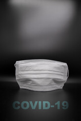 white disposable mask in corona times with black background and inscription covid-19 and free text space