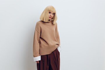 Fototapeta premium Horizontal photo, a woman on a white background in a beige sweater and brown trousers with beautiful blond hair is standing