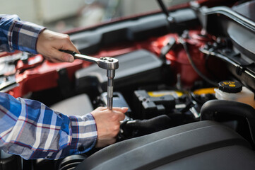 Fototapeta na wymiar Female auto mechanic unscrewing a nut to replace a car spark plug.