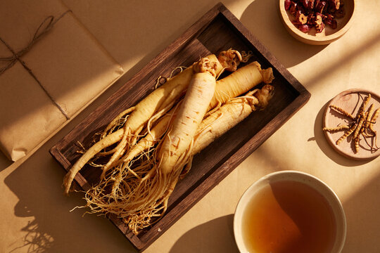 Fresh ginseng wooden tray with side braided tonic basin, cordyceps tray, and red dried apple bowl with a golden paper background.