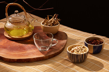 A seed bowl is exhibited on a bamboo table alongside the teapot, cup, and bowl of dried herbs on a wooden pedestal.
