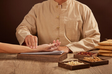 The old doctor of traditional Chinese medicine to the patient's pulse with wooden tray of herbs...