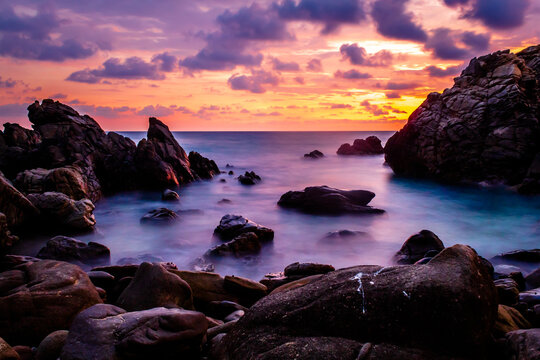 sunset on the beach  with sky full of colors and purpple clouds, rocks in the waves, long exposure photo in puerto escondido, oaxaca 