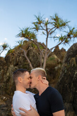 Fototapeta premium gay couple kissing and smiling with rock and trees in background