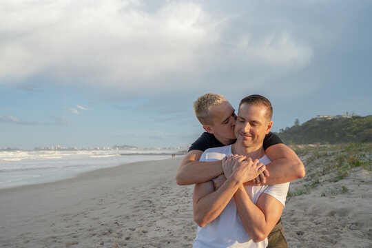 gay couple cuddle from behind on beach with eyes closed