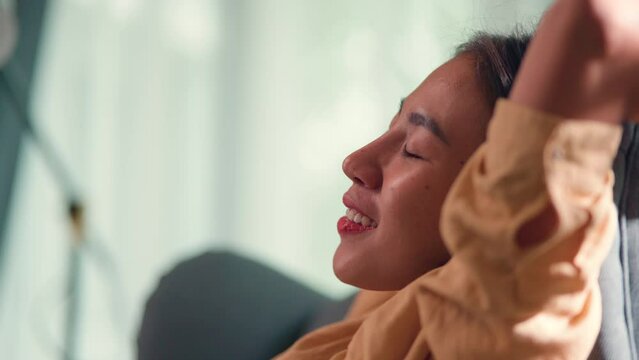 Side view, Close up face of Young asian woman sitting on sofa, she smile and close her eyes with feel comfortable and happy after finish work, new normal and working from home concept