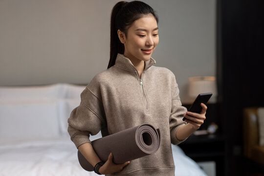 Young woman holding yoga mat and smartphone