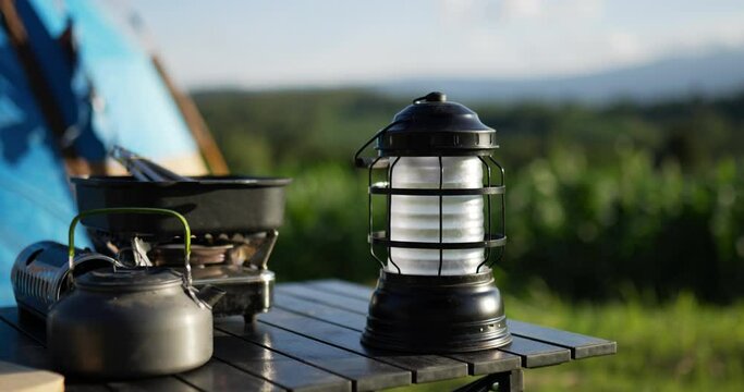 Handheld panning shot, The Camping equipment consists of lantern, gas stove, kettle and pan on table in front of tent. Family camping concept