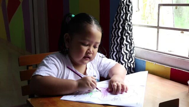 Adorable asian little girl enjoying her activity. Preschooler coloring or drawing on her book at home