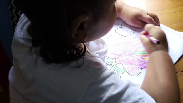 Back view of asian little girl coloring anggrek or ochid picture on her book