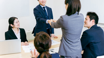 商談で契約成立して握手するスーツ姿の男女
