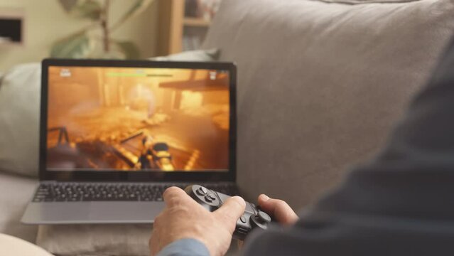 Unrecognizable gamer playing fps game on laptop with gaming controller at home