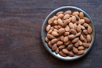 Almonds in a ceramic plate on a dark wooden floor, flat lay, space for text.