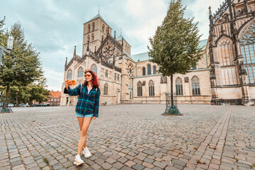 Happy tourist girl taking selfie photo while visiting St. Paulus Dom Cathedral and admiring old town architecture buildings in Munster, Germany