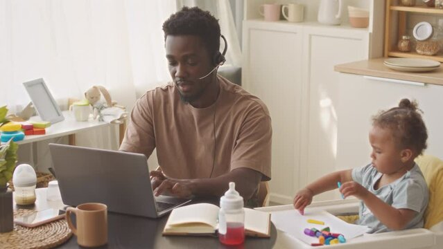 Black man with toddler daughter working in call centre from home, trying to concentrate on work while girl distracting him