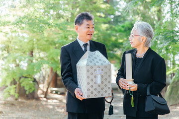 お葬式で火葬した遺骨を持つ日本人の高齢者夫婦
