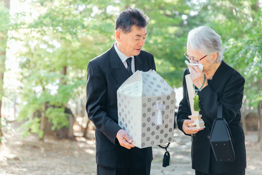 お葬式で火葬した遺骨を持つ日本人の高齢者夫婦
