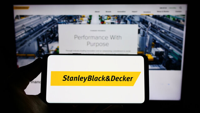 Stuttgart, Germany - 10-15-2022: Person holding cellphone with logo of American tools company Stanley Black and Decker Inc. on screen in front of webpage. Focus on phone display.