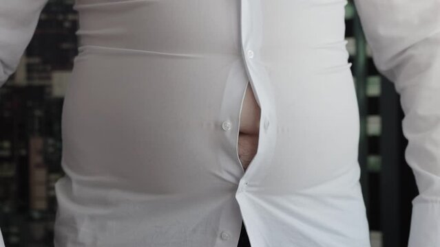 A man's shirt buttons are unbuttoned on his stomach due to a fat belly and obesity. Tight clothes, overweight. Slow mo