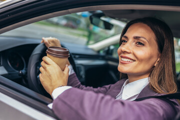 Young businesswoman driving in a car to work with her arm leaning out of the vehicle during the day, drink coffee.