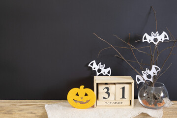 Decorative composition for Halloween. A calendar, a pumpkin, a vase with branches, with flying mice stand on the table against a black wall. Space for your text. High quality photo