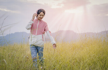 Young teenager girl enjoy listening to music with headphone with feeling happy and relaxed on mountain park sunset background
