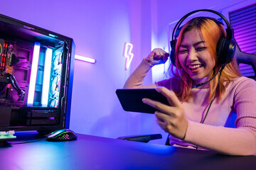 Winning. Happy Gamer playing video game online with smartphone with neon lights she raises hands to...