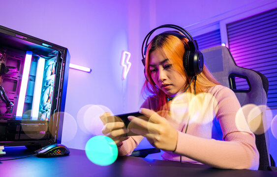 Losing. Gamer in playing video game online with smartphone with neon lights she fail game over, confused Asian woman wearing gaming headphones play mobile phone feeling shocked disappointed at home - Powered by Adobe