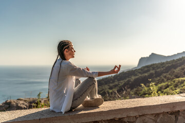 Fototapeta na wymiar Profile of a woman doing yoga in the top of a cliff in the mountain. Woman meditates in yoga asana Padmasana