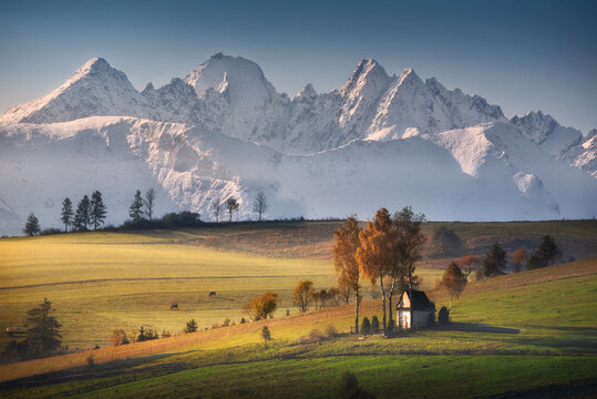 Kaplica Matki Boskiej śnieżnej w Kacwinie na tle panoramy zimowych Tatr. Jesień, Polska. 
The chapel in Kacwin against the backdrop of the winter Tatra Mountains panorama. Autumn, Poland.