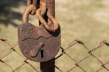 Old rusty padlock next to wire fence door closeup