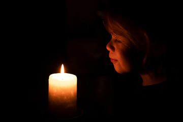 little girl smiling looking at burning candle in a dark room. child blowing out the candle. light...