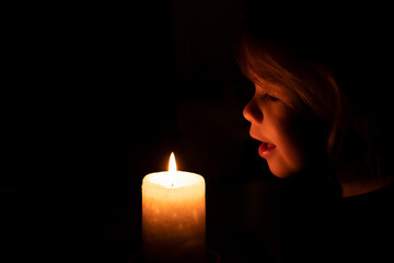 child blowing out a candle flame. little girl looking at burning candle in a dark room. light in darkness