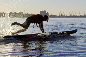 Fototapeta premium Man doing beach start on SUP on rowing competitions from stand up paddle boarding. River beach start on SUP