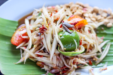 Spicy thai papaya salad  with salted crab and fermented fish (Som Tam Poo Plara) in green banana leaf on plate table background