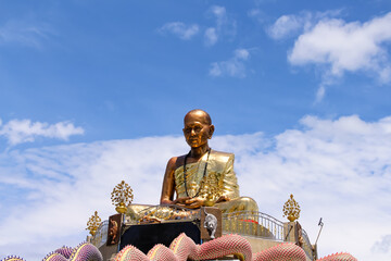 Obraz premium Gold Kruba Sriwichai statue seat image on bright blue sky background at Wat Phra Pan(Phra Non Mae Puka temple ) of san Kamphaeng in Chiang Mai of Thailand