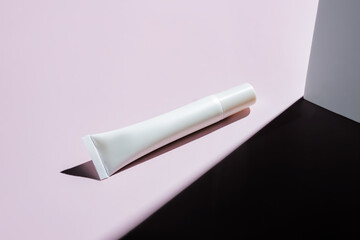 White unbranded plastic tube with eye cream or face serum on pink background with hard shadows. Mockup for skin care products