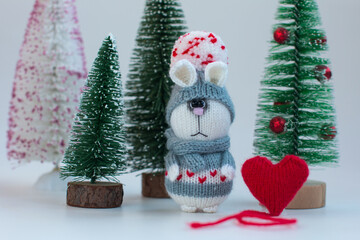 Knitted bunny with gifts on a wooden background with a Christmas tree. New Year of the hare 2023, handmade