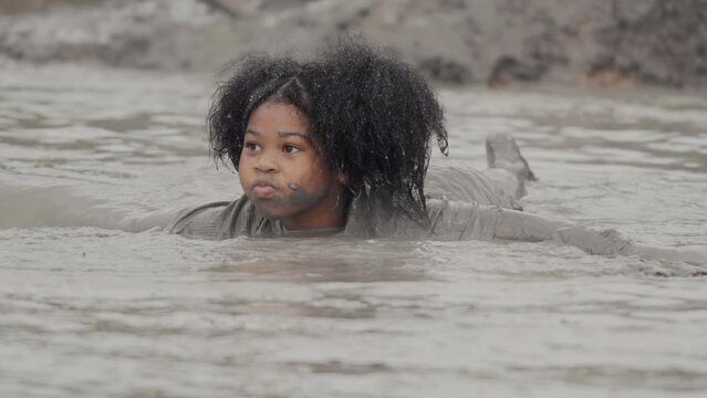 Happy child girl laying and playing in large wet mud and dirt on summer day