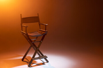 The director's chair stands in a beam of light with an orange backlight and smoke. Place for text....