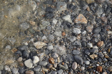 Sunny autumn day on the shores of the Aegean Sea. Texture of wet pebbles on the sand of the beach. Surf. Glare on the water. On the edge of the elements