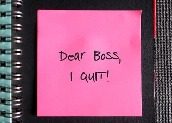 Bright pink note on black notebook page with text handwriiten DEAR BOSS I QUIT , concept of decision to resign or quit from job