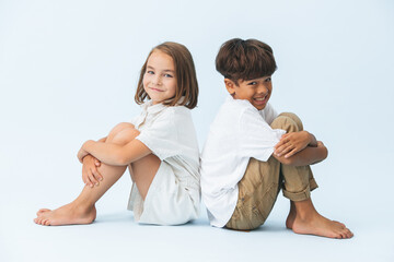 Fun portrait of awkwardly smiling boy and girl sitting back to back on the floor
