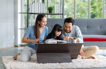 Millennial Asian happy family father and mother sitting on cozy carpet floor smiling helping teaching little young girl daughter reading studying learning with big textbook in living room at home