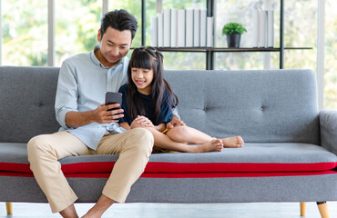 Millennial Asian happy family father sitting smiling on cozy sofa couch holding showing funny...