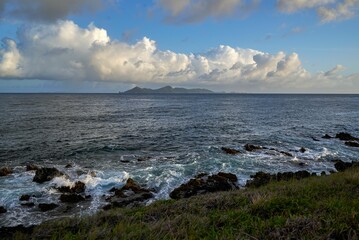 Gorgeous view of the sea with low tides washing over rocks under a grassy hill on a sunny day