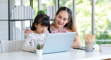 Millennial Asian happy family mother smiling helping supporting teaching little girl kid daughter studying learning doing online school homework via laptop notebook computer in living room at home